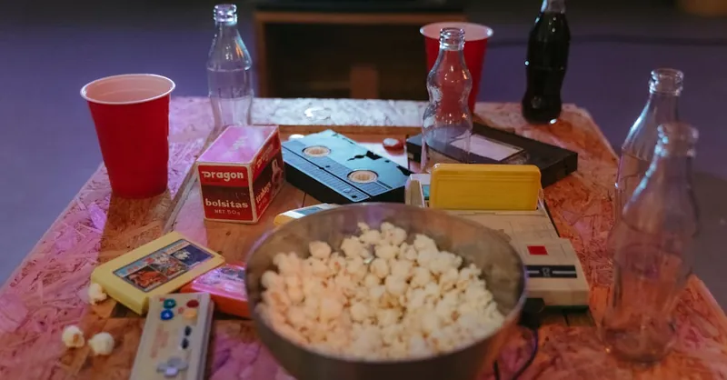 A nostalgic setup with popcorn, VHS tapes, and retro gaming consoles on a wooden table.