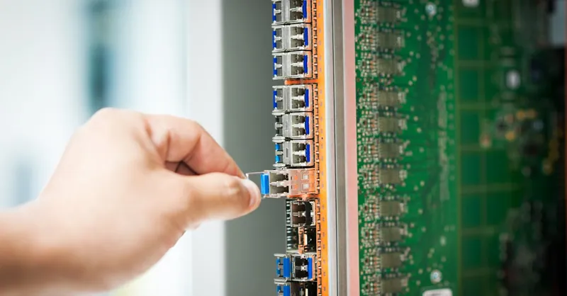 An individual connecting a cable into a network server port indoors, focusing on technology setup.