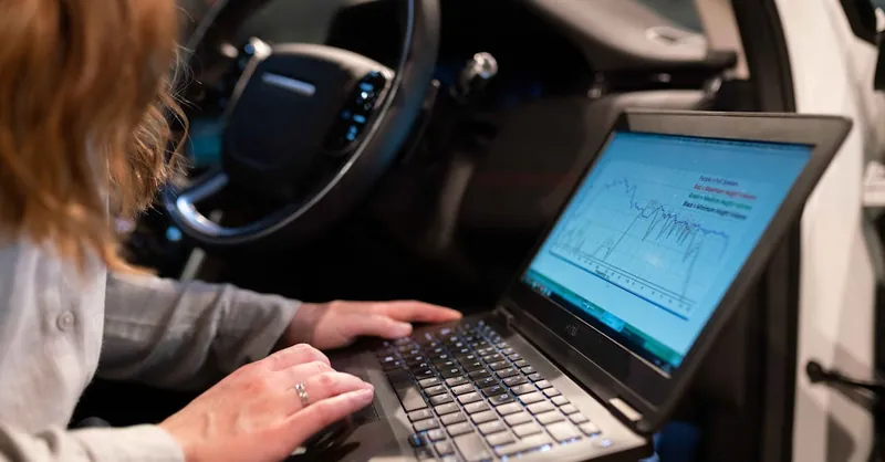 Female engineer using laptop to analyze vehicle data inside a car for testing purposes.