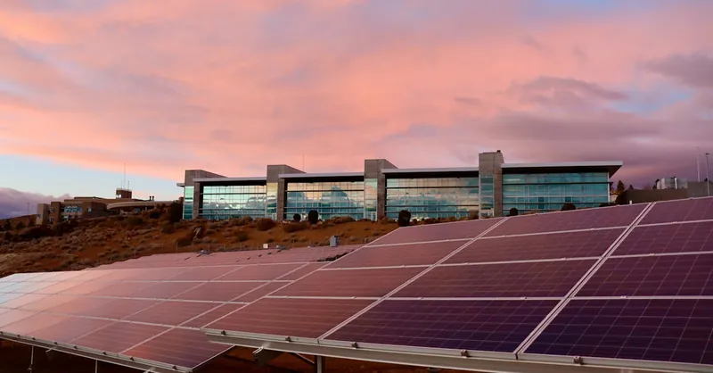 Solar panels in front of a modern building at sunset showcasing renewable energy technology.