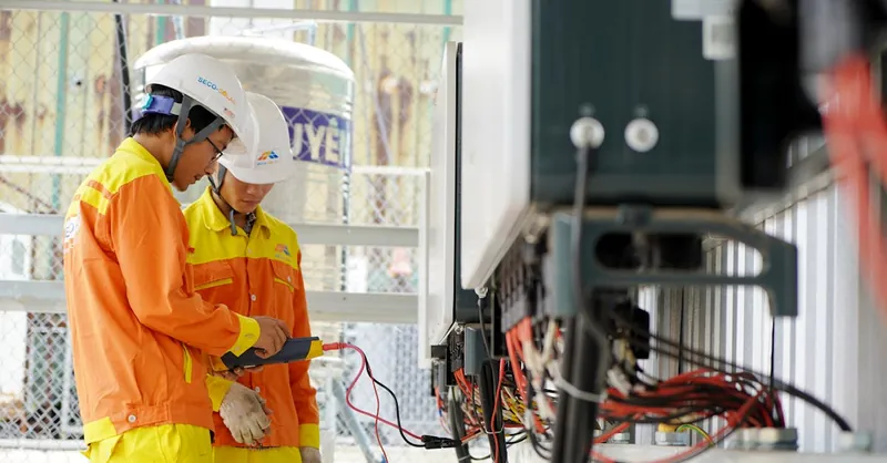 Two technicians with helmets working on electrical equipment outdoors, ensuring safety.