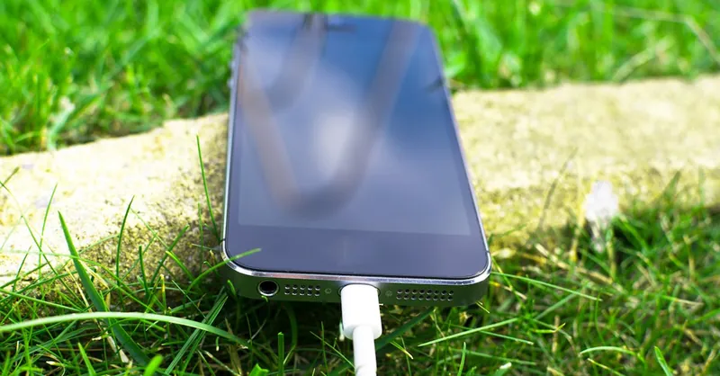 Close-up of a smartphone charging on a grassy lawn, highlighting modern technology in nature.