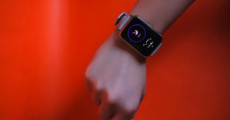 Fist wearing a smartwatch with fitness tracking display on a vibrant orange background.