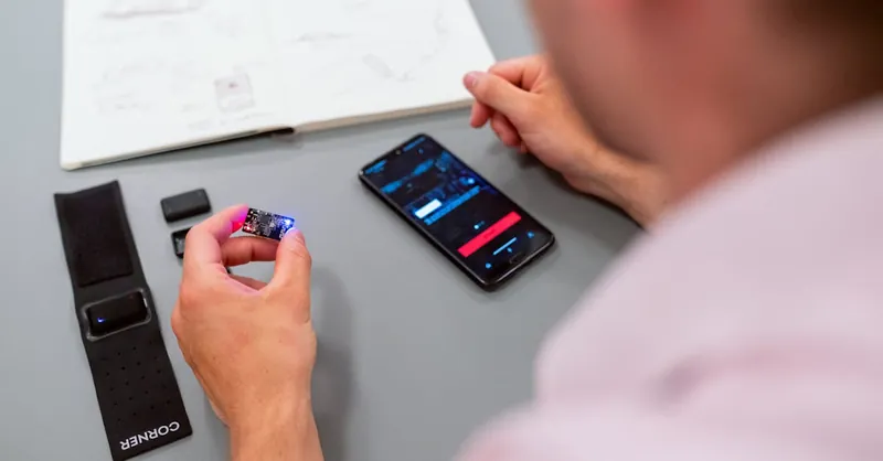 Engineer testing a wearable prototype using a smartphone interface at a desk.